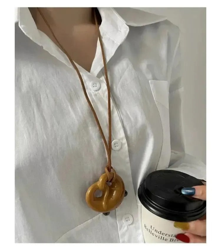 A person wearing a white shirt and holding a coffee cup is wearing a brown leather necklace with a heart-shaped pendant.
