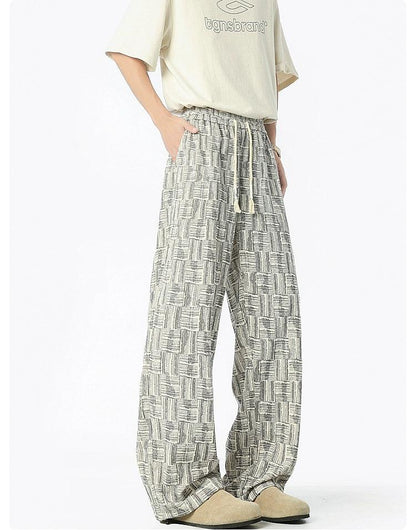 A person wearing a white t-shirt and patterned wide-leg pants stands against a white background.