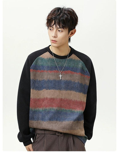 A young man with short dark hair wearing a striped sweater and a cross necklace stands against a white background.