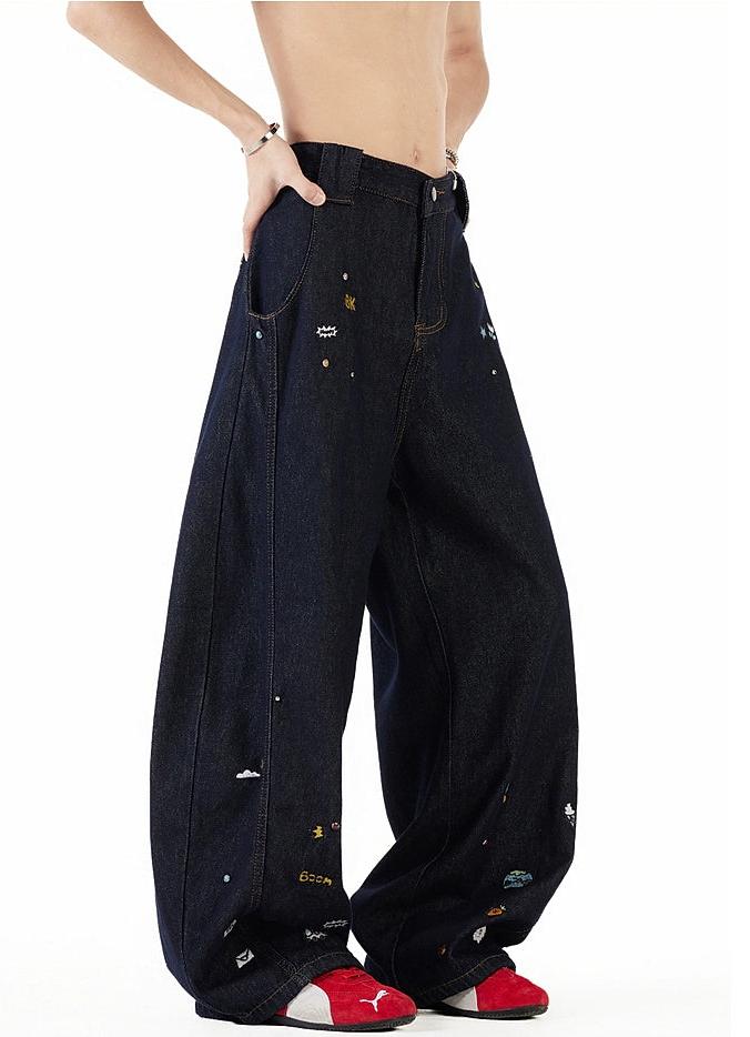 A person wearing a pair of wide-leg, dark blue jeans with various colorful designs and patches on them, paired with red shoes.