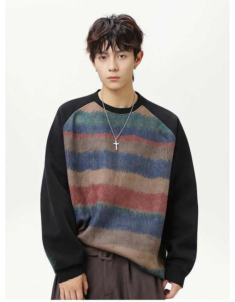 A young man with dark hair wearing a striped sweater and a cross necklace stands against a white background.