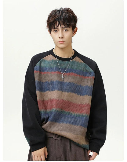 A young man with dark hair wearing a striped sweater and a cross necklace stands against a white background.