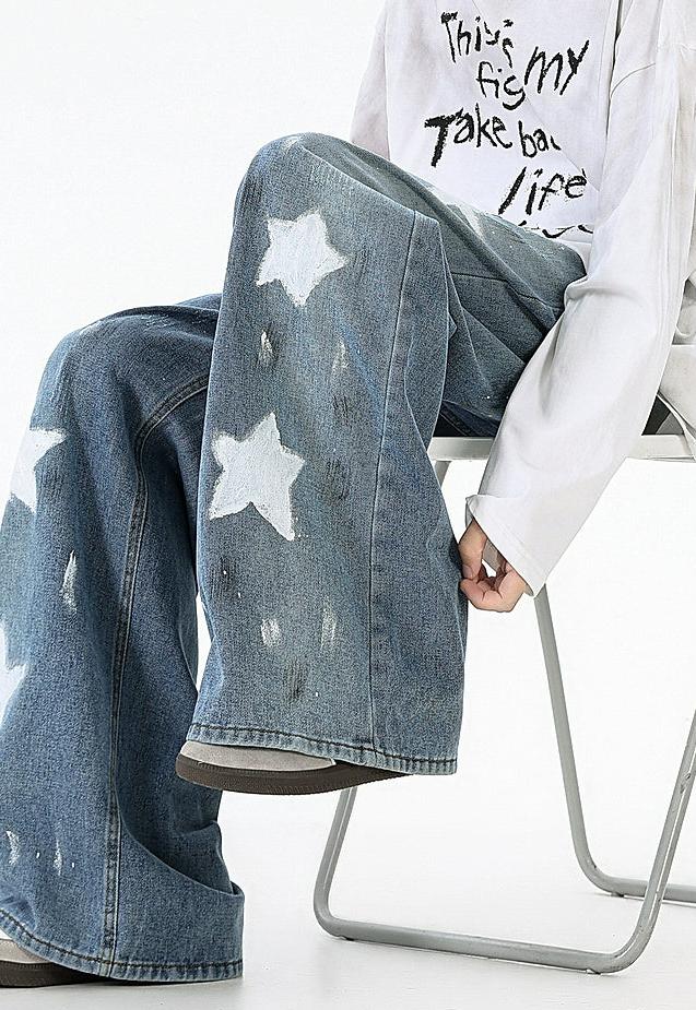 A person sitting on a chair wearing a white shirt with black text and blue jeans with white star designs.