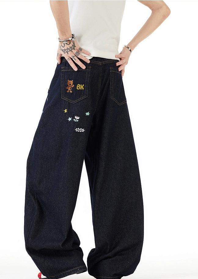 A person wearing a white shirt and black jeans with various designs and characters on them.