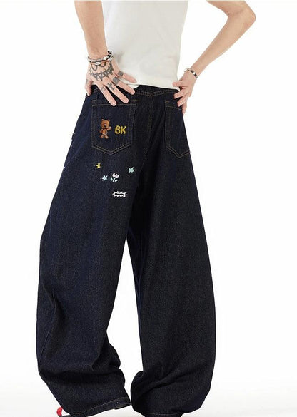 A person wearing a white shirt and black jeans with various designs and characters on them.