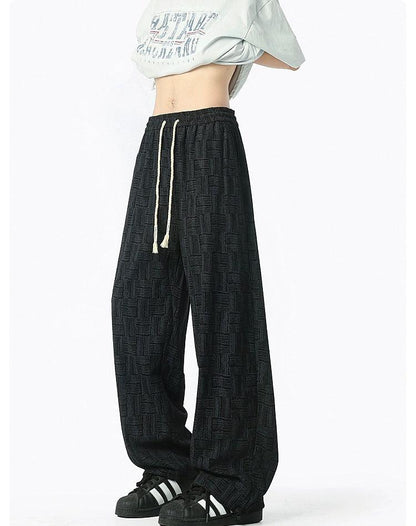 A person wearing a white shirt with a graphic design and black patterned pants stands against a white background.