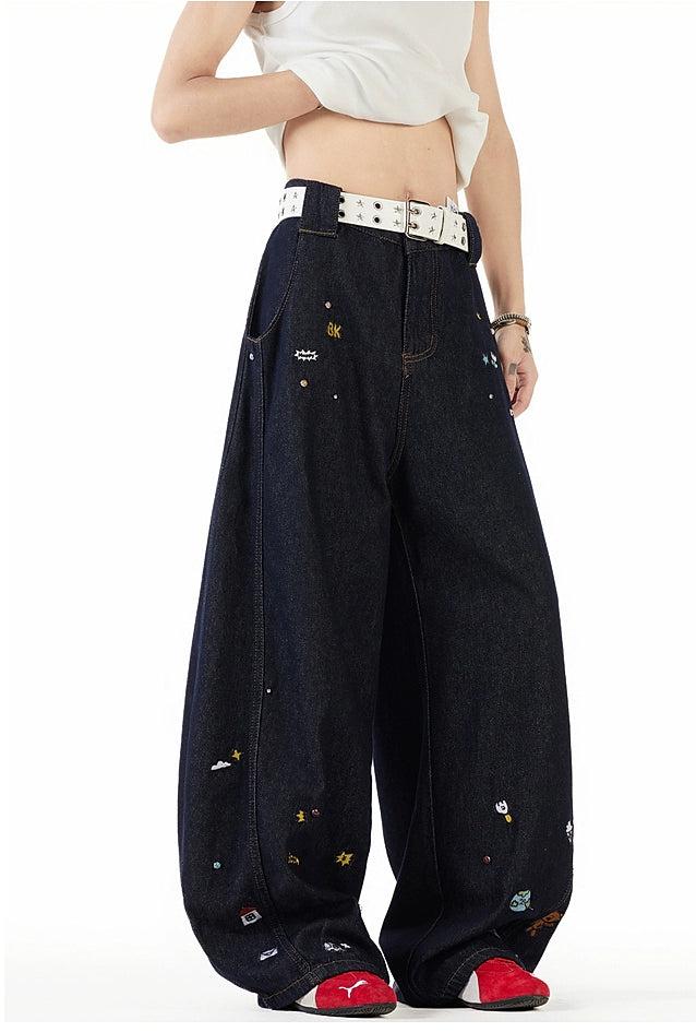 A person wearing a white top and wide-leg jeans with various colorful designs and patterns.