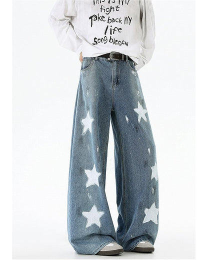 A person wearing a white sweatshirt with black text and blue jeans with white star patterns.