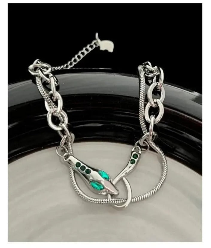 A silver necklace with a snake-shaped pendant and green gemstones.